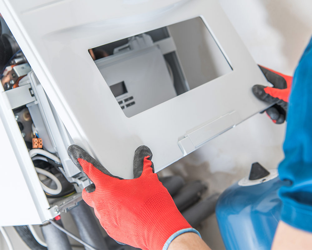 A man wearing a blue shirt and red gloves repairs a water heater, demonstrating hands-on maintenance skills.