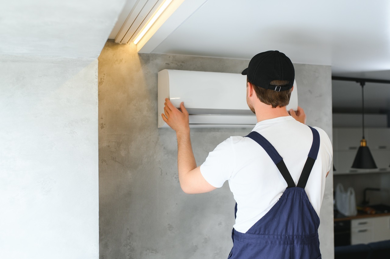 A man in overalls repairs an air conditioner, demonstrating his skills in home maintenance and appliance repair.