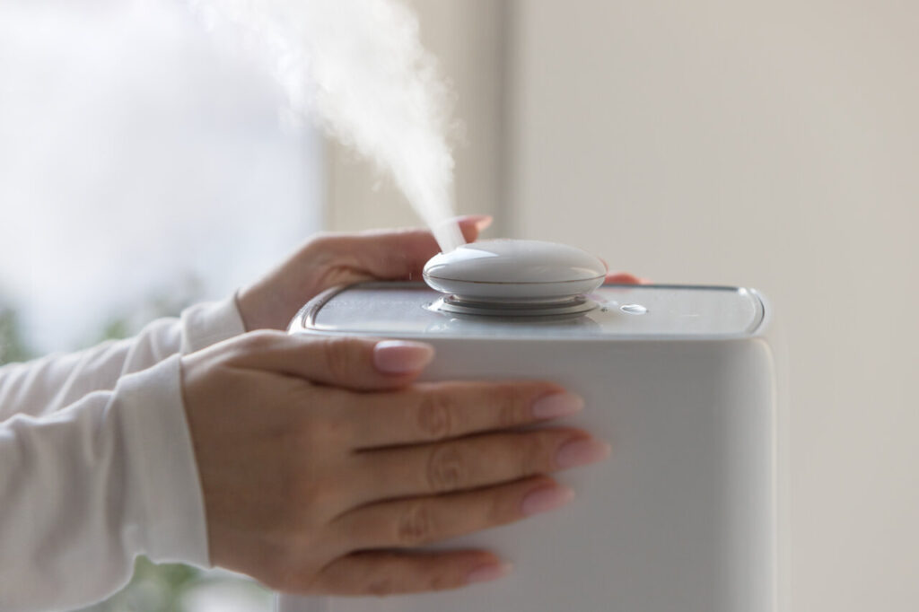 A person operates a humidifier, releasing a gentle stream of steam into the air for improved humidity levels.