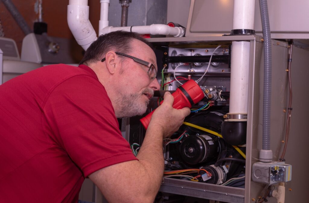 A man in a red shirt diligently working on a furnace, focused on his task in a workshop environment.