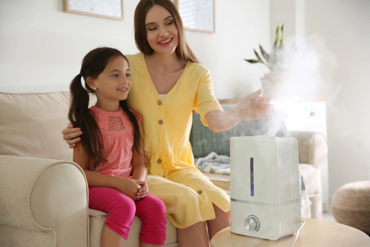 A mother and daughter are using a humidifier together in their cozy living room, enhancing their comfort and well-being.